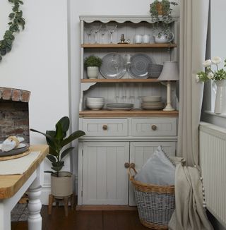 White painted storage dresser next to a fire place, decorated with cutlery, plants and a lamp
