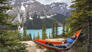 Camper sleeping in hammock with lake and mountain behind