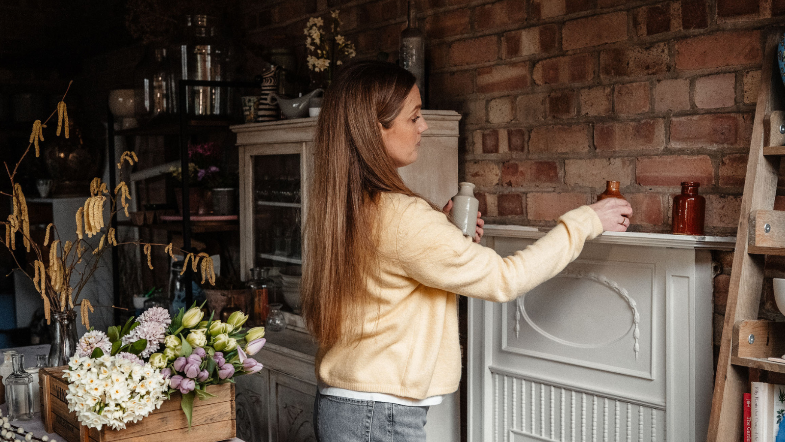 Woman placing ceramic ink wells on a mantelpiece in floristry workshop