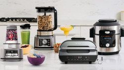 A kitchen bench with lots of Ninja appliances on it including a blender, slow cooker and grill press