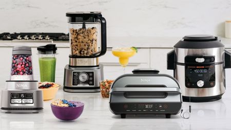 A kitchen bench with lots of Ninja appliances on it including a blender, slow cooker and grill press