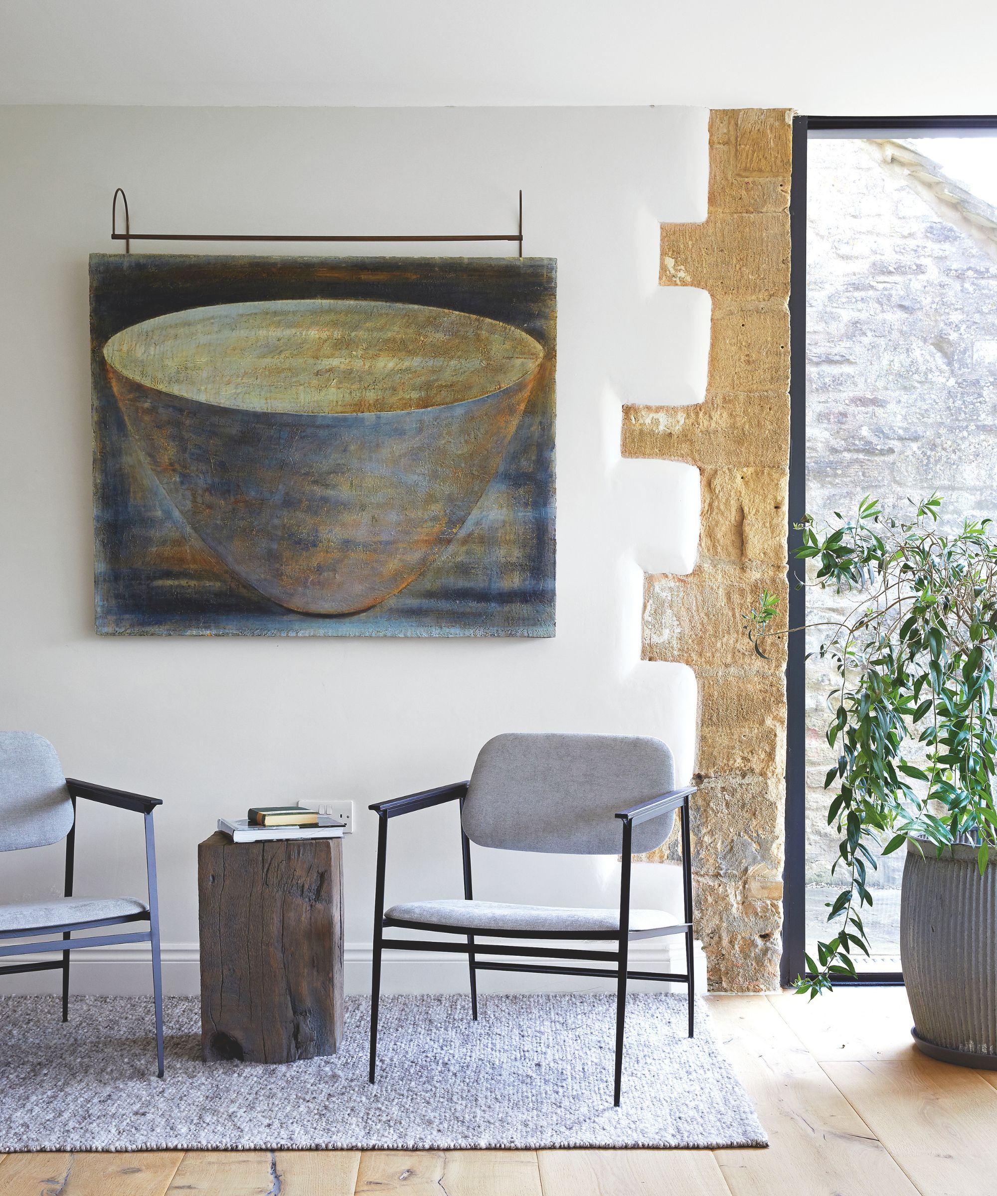 Minimal living room with large painting, two chairs, wood side table and large plant