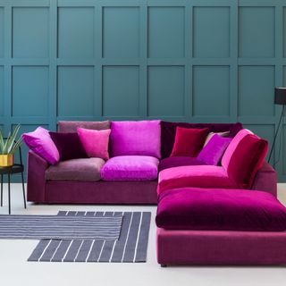 living room with teal wall and white flooring with wine colour sofa set with colourful cushions