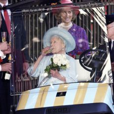 The Queen Mother drinking champagne while being driven around in a buggy as staff members drink champagne next to her