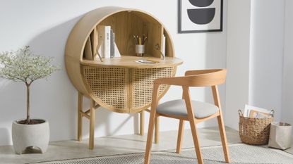 Round rattan and wood desk in modern living scheme with potted tree, natural woven storage basket, and abstract wall print.
