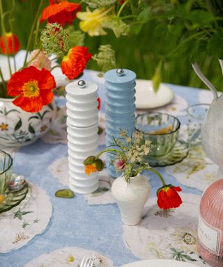 An outdoor dining table with blue and white salt and pepper shakers and small floral arrangements