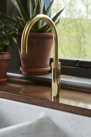 A gold hot water tap on a walnut wood countertop