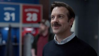 A screenshot of Ted Lasso smiling in the locker room during the pilot of Ted Lasso.