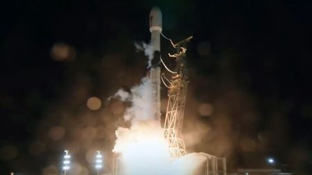 a black and white rocket lifts off its launch pad with a bright white thrust into the dark night sky