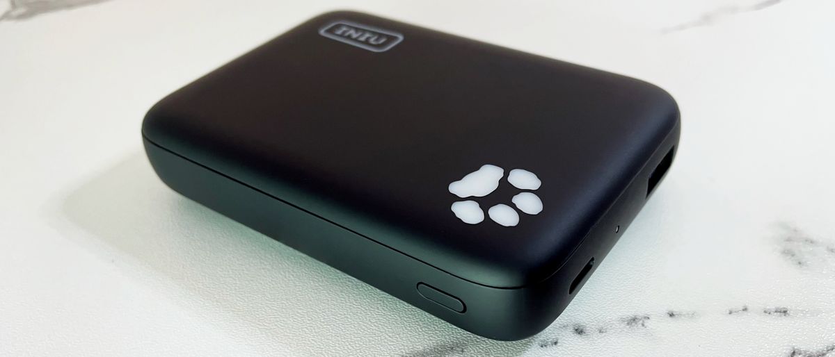 The INIU B43 power bank sits on a marble-effect surface, with the paw print-shaped light angled slightly toward the camera.