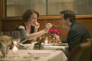 A man and woman are enjoying a romantic meal in a resturant. The woman is sharing her food with the man.