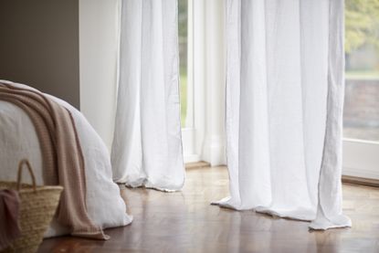 How to hang curtains without drilling: bedroom with white linen curtains trailing on the wooden floor