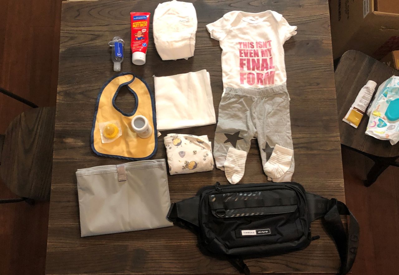 Cross body bag on table with various baby items.