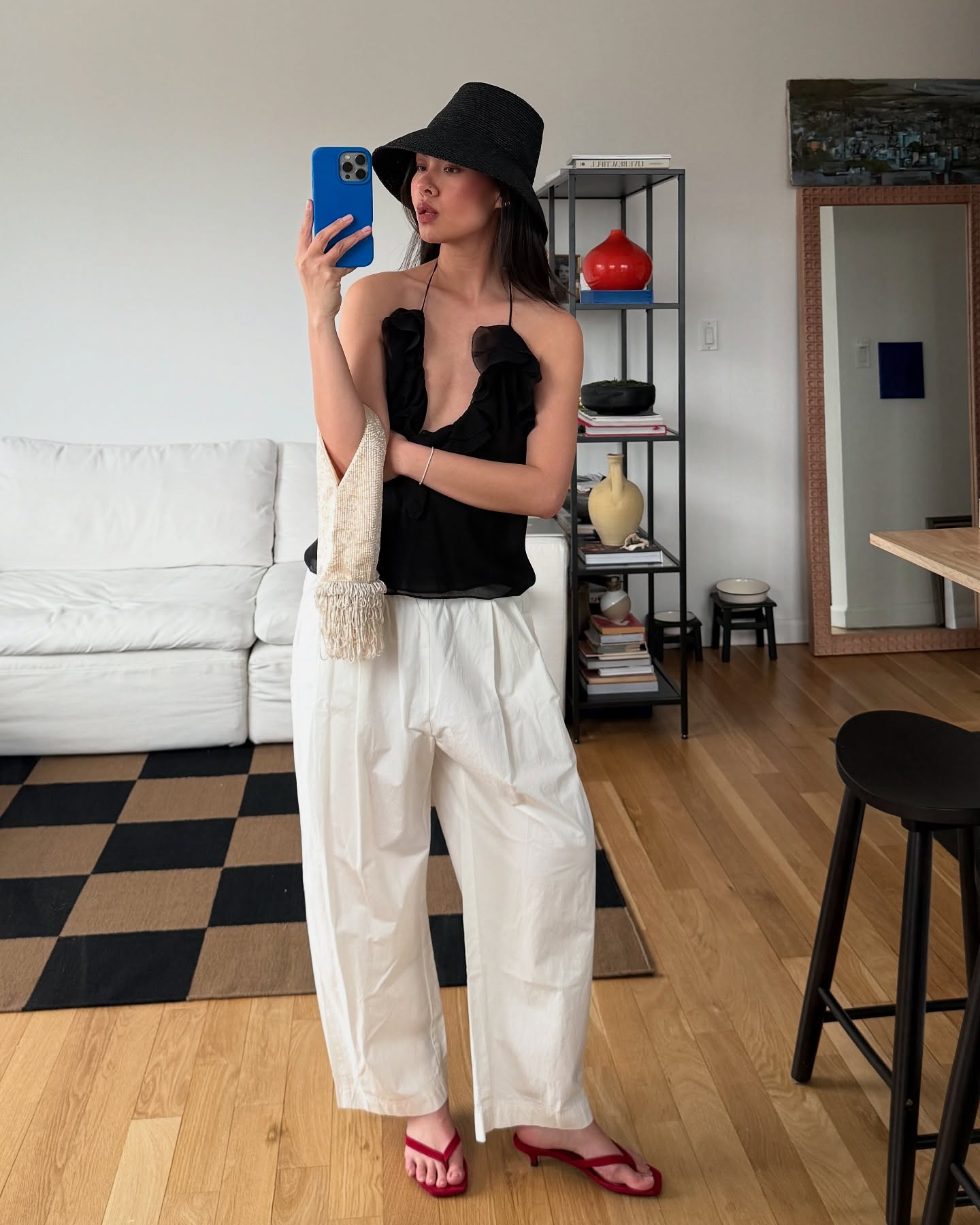 Mimi Nguyen wears a black cami top, white trousers, red thong sandals, a beaded bag and black woven hat.