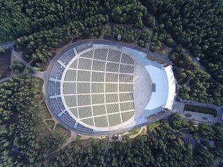A birds-eye view of the National Open Air Stage with a forest surrounding it. The shape of the structure is similar to that of a horse-shoe.
