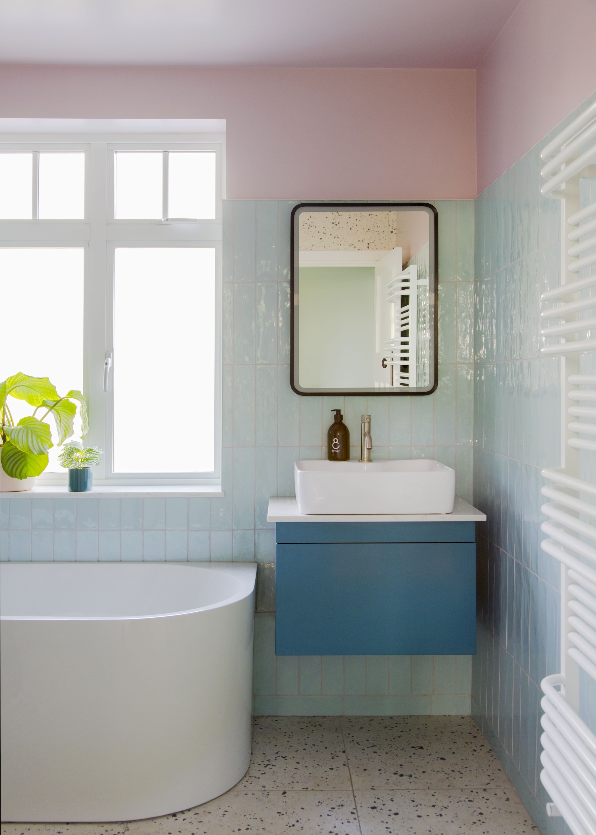 A colorful bathroom with hues of baby blue and light pink. There is a corner view of a large bath tub and you can also see a blue vanity with a basin.