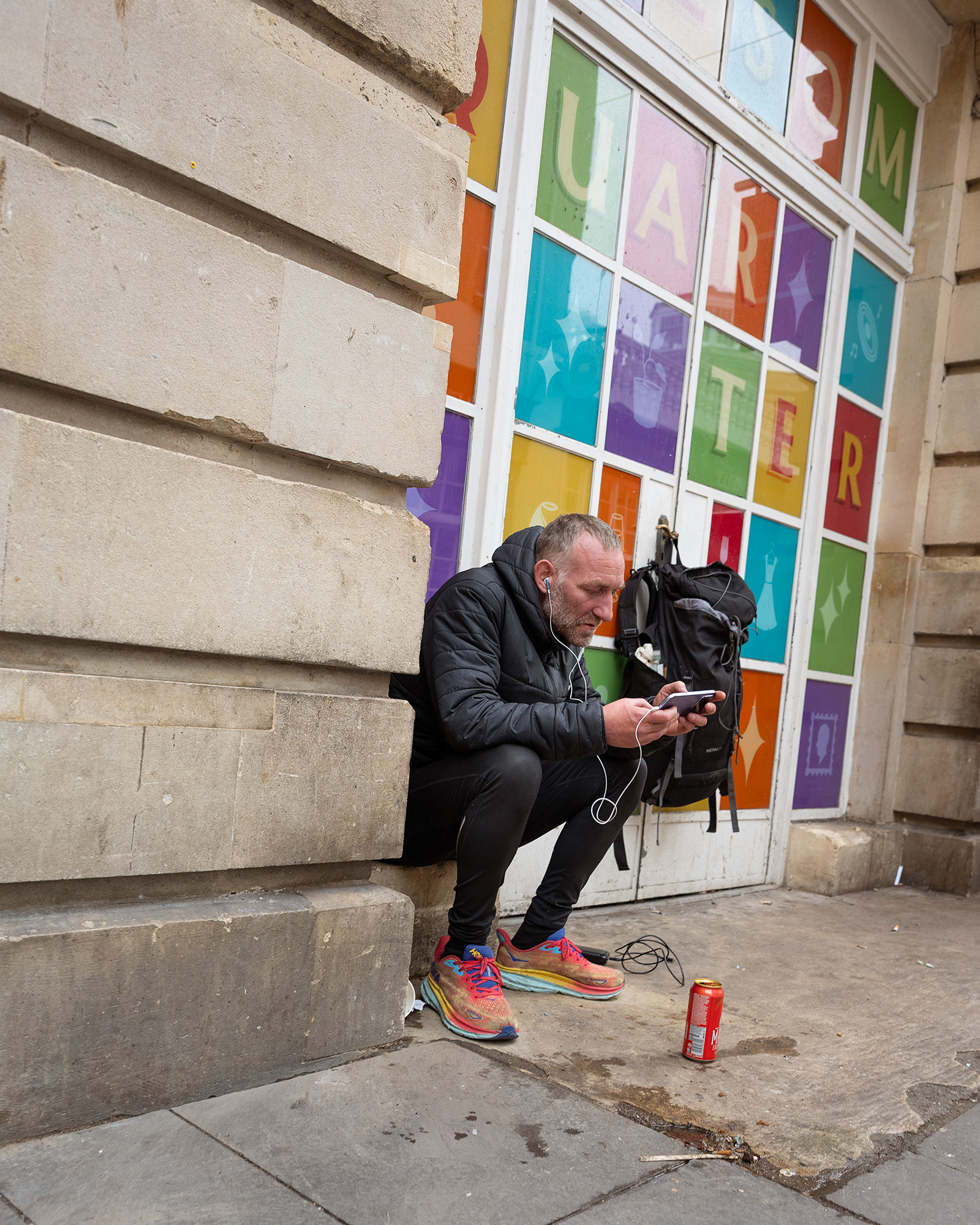 Street photograph of man on phone sat by colorful window