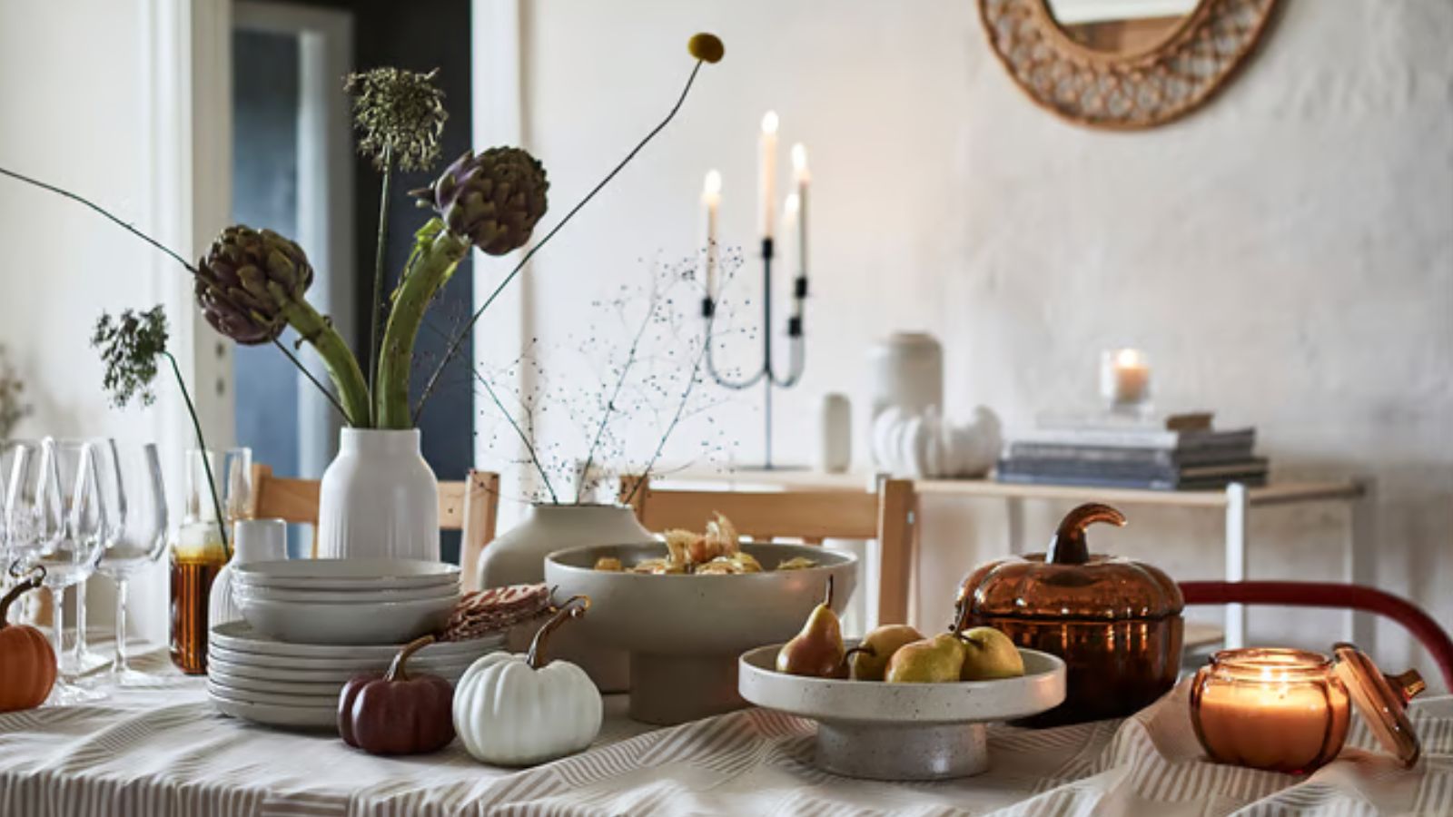 Table with stacks of plates, vase with stems, and pumpkin decor and neutral tablecloth