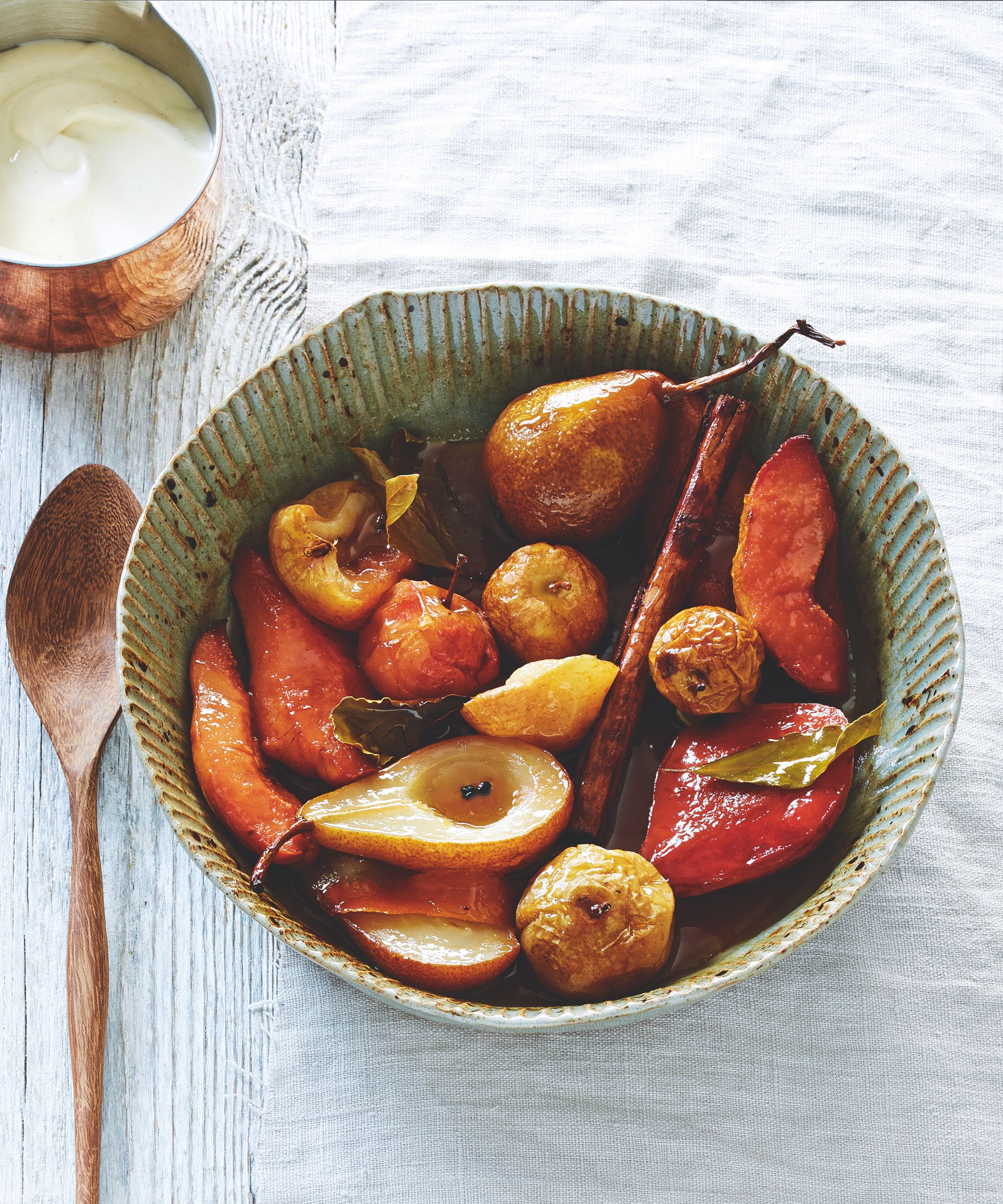 Baked fall fruits in a rustic bowl with wooden spoon and copper jug of cream beside