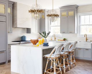 Marble kitchen island with duo of statement glass and brass chandeliers hanging above