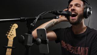 A man sings into an IK Multimedia iPhone microphone with a guitar in the background