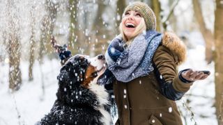 Woman with her faced turn toward the sky laughing with her Bernese Mountain Dog as they enjoy the snow falling