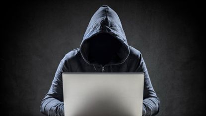 A stock photo of a man in a hood using a laptop.