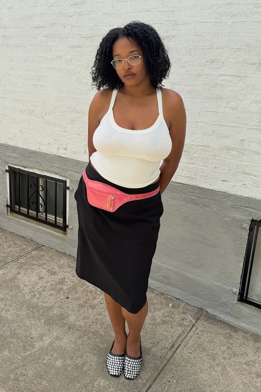 A woman wearing a tank top, pink utility belt, and black skirt.