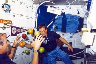 two astronauts play with fruit in microgravity aboard the space shuttle