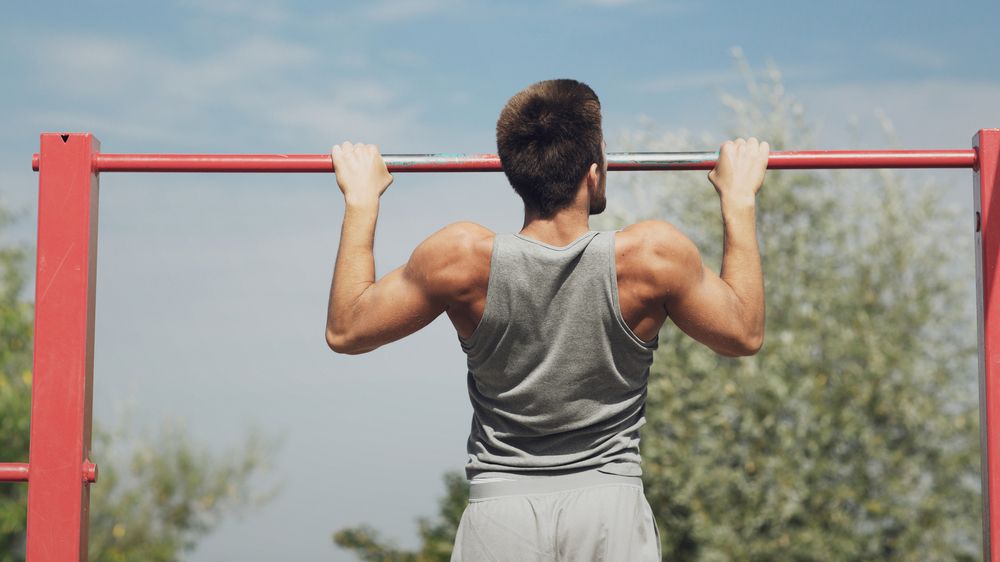 Man performs a pull-up on a bar outside