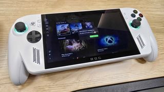 ROG Xbox Ally on a wooden table displaying the game launcher menu. A pop up in the center says, "Your battery is running low. You might want to plug in your PC."