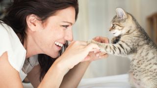 Smiling woman playing with her cat — this is one of the best tricks to teach your cat 