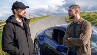 Joe and Shaun stand together next to a car on the road.