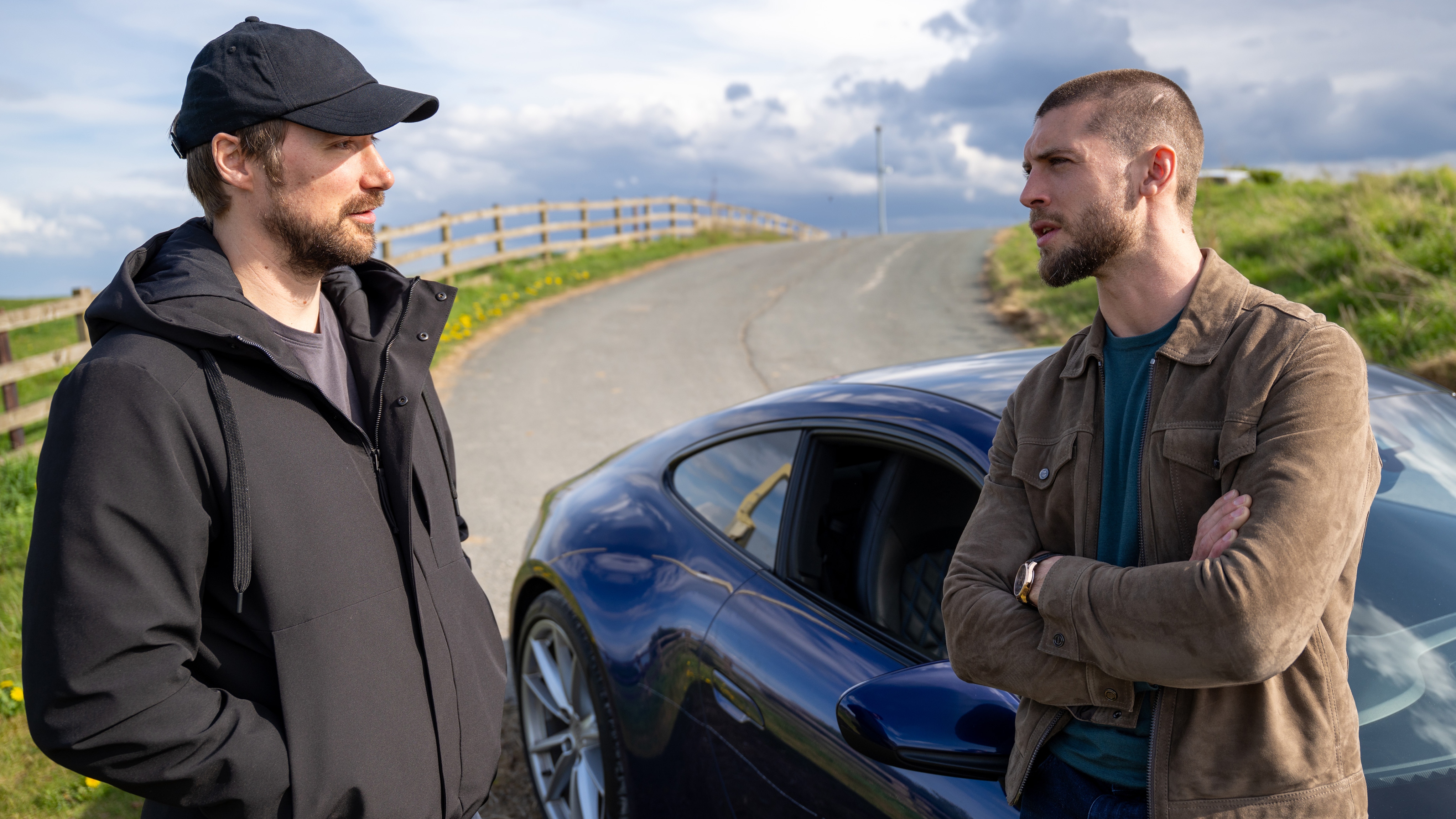 Joe and Shaun stand together next to a car on the road.