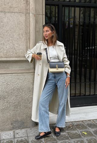 a photo of a woman's classic outfit idea with a trench coat over a t-shirt, jeans, and ballet flats