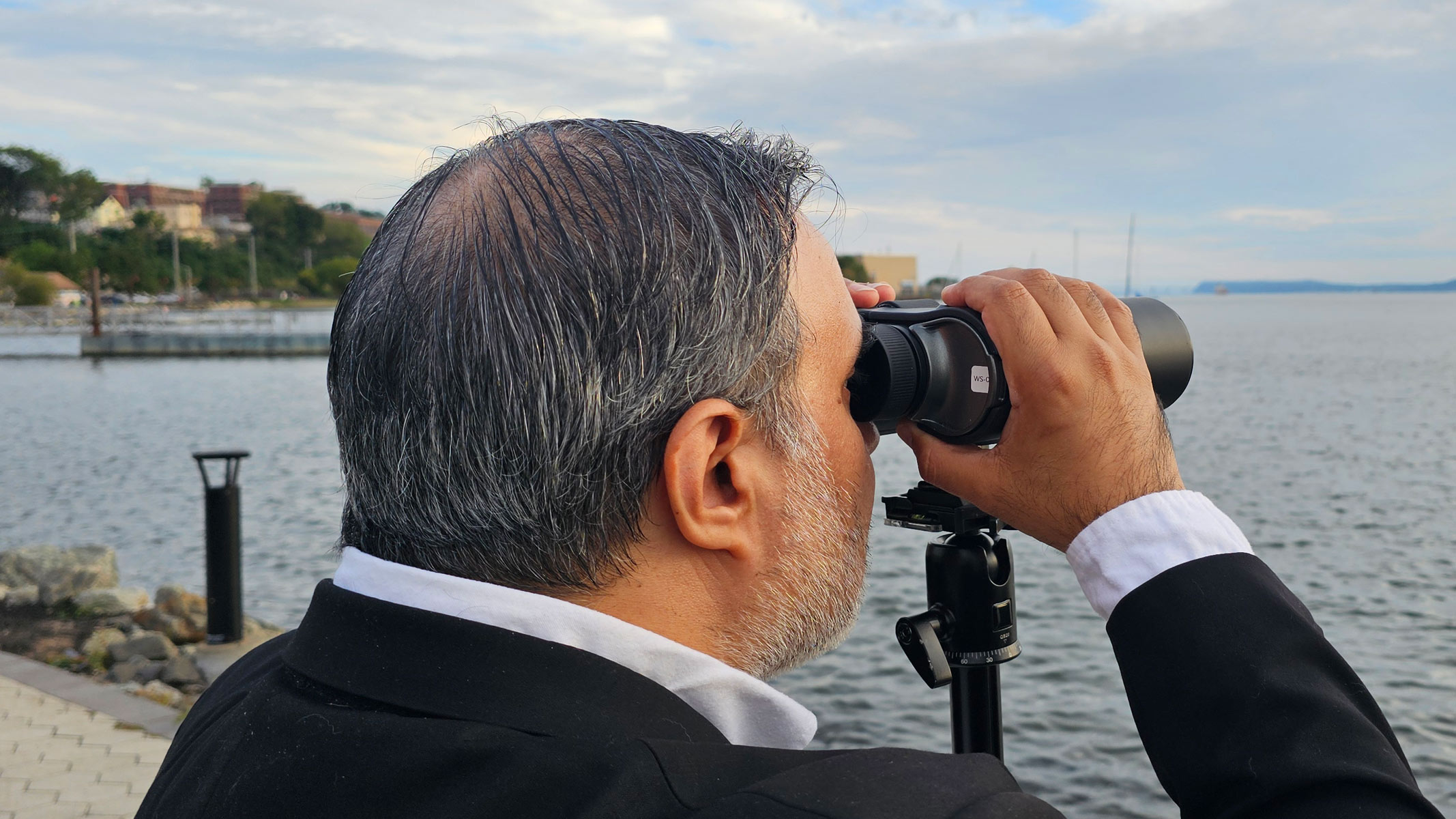 A man looking through the Unistellar Envision smart binoculars with water in the background.