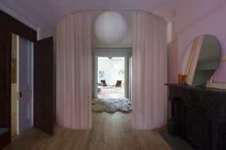 A room with a circular pink curtain, which is open and looking through to a hallway with a rug and a patio area.