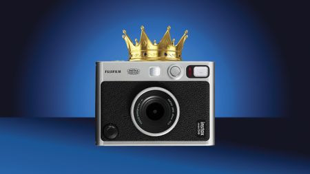 A silver Fujifilm Instax Mini Evo camera adorned with a golden crown, set against a gradient blue background