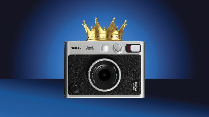 A silver Fujifilm Instax Mini Evo camera adorned with a golden crown, set against a gradient blue background
