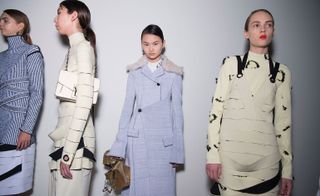 Four models, one wearing a black and white top, two with cream tops with black detailing, and one wearing a pale blue coat