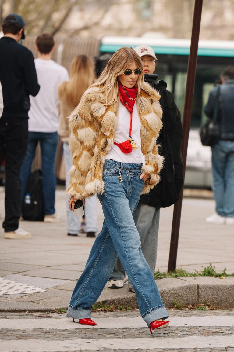 A woman wears a fur coat, white tee and baggy jeans to Paris fashion week