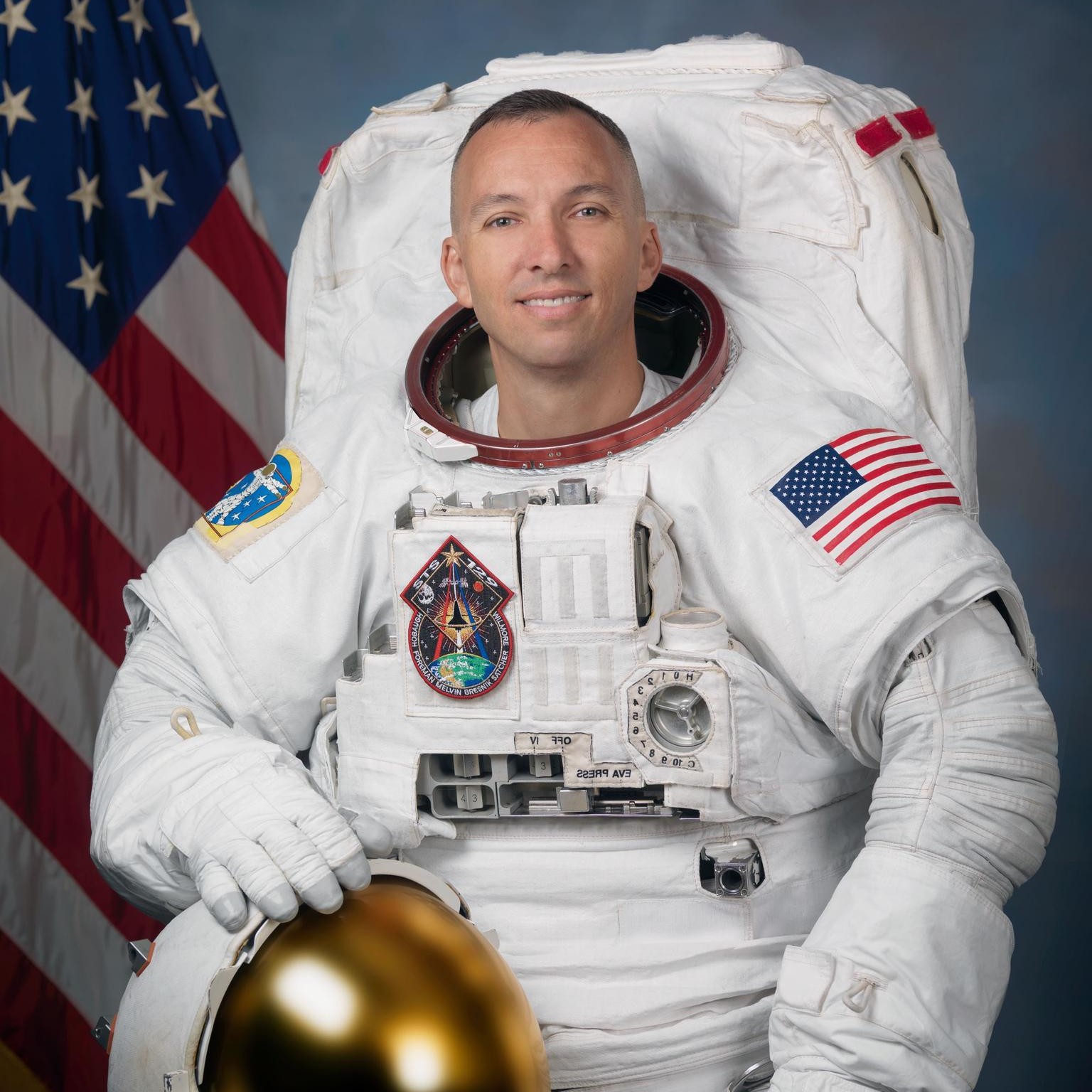a man in a blue flight suit poses for a portrait