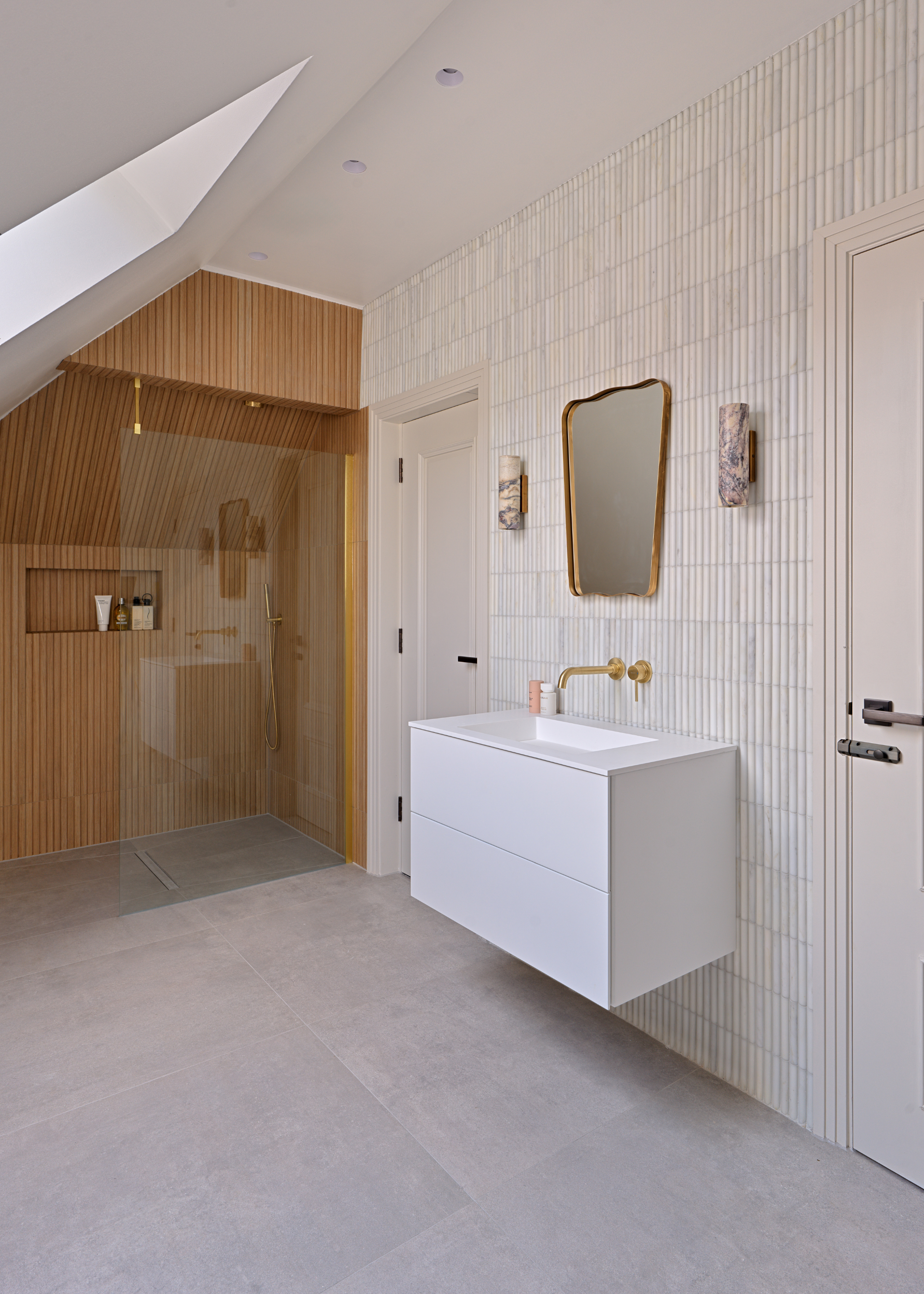 A spa-like bathroom with a wooden effect zoning the shower area, a modern wall hung vanity unit in white with brass hardware and mirror above