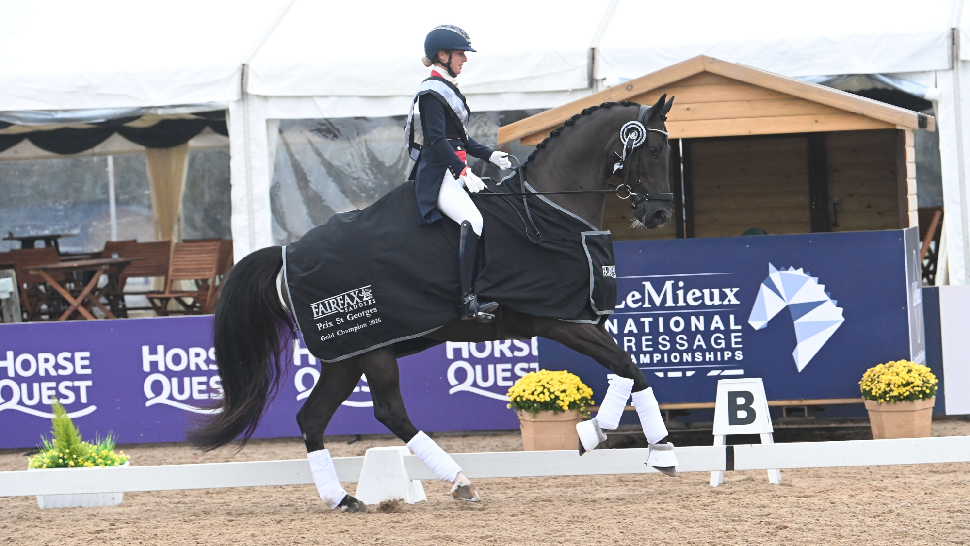 Laura Tomlinson in her British team navy and red tailcoat, wearing a winner&amp;rsquo;s sash, riding on Ostmarks Digal in a prize-giving at the 2026 National Dressage Championships