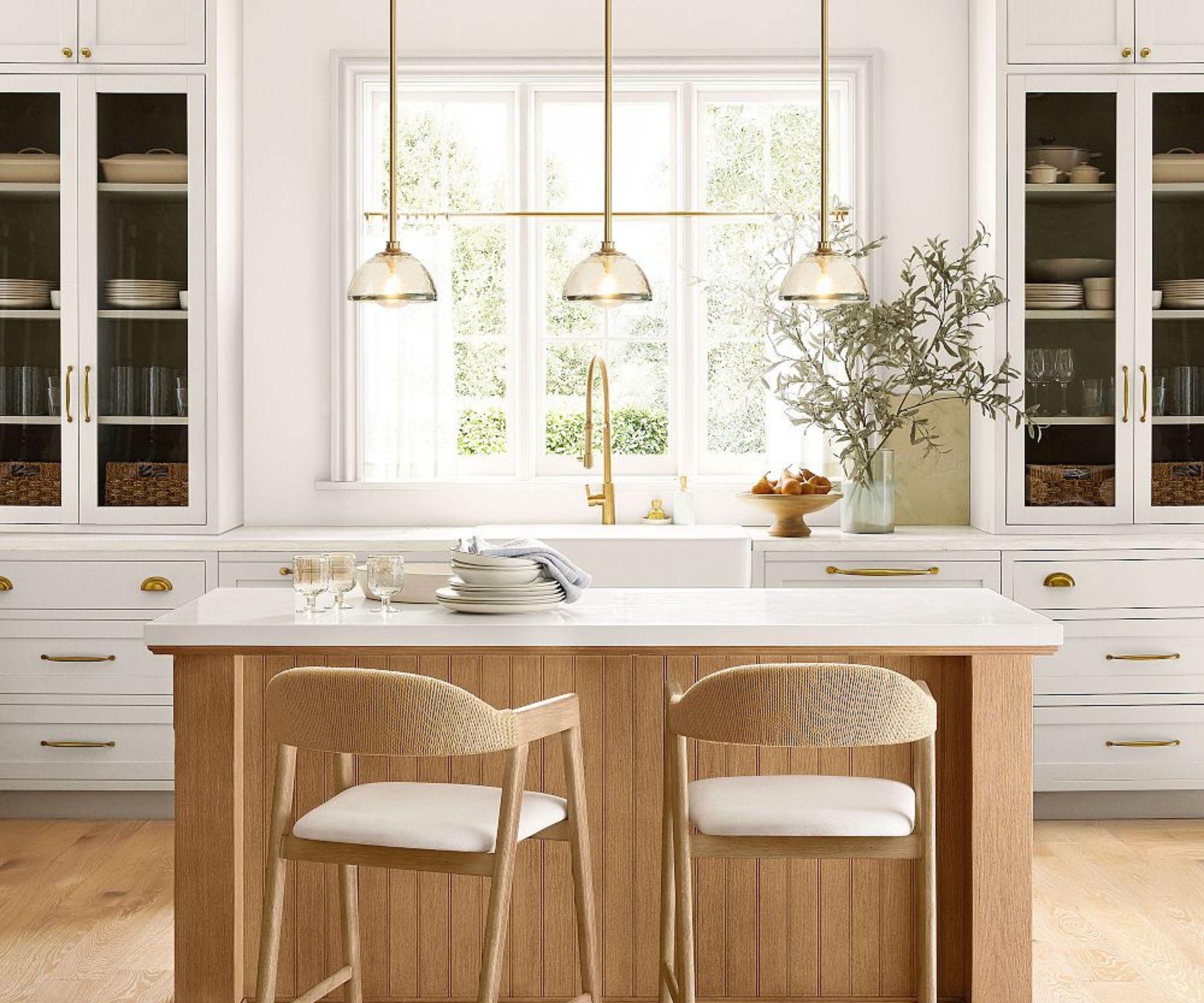 A white kitchen with a wood island and brass pendant lights