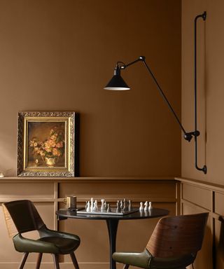 A room painted with rusty brown paint, with a chess table, sconce and vintage picture frame