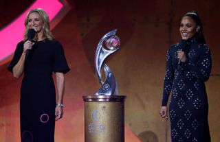 Host's Gabby Logan MBE and Alex Scott MBE smile on stage alongside the UEFA Women's Euro Trophy during the UEFA Women's EURO 2022 Final Draw Ceremony on October 28, 2021 in Manchester, England. 