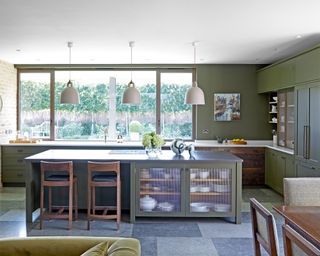 green kitchen with exposed brick wall, green cabinets and island, trio of pendant lights and dining table and chairs