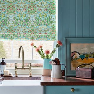 green patterned roman blind over window above kitchen sink and panelled blue walls