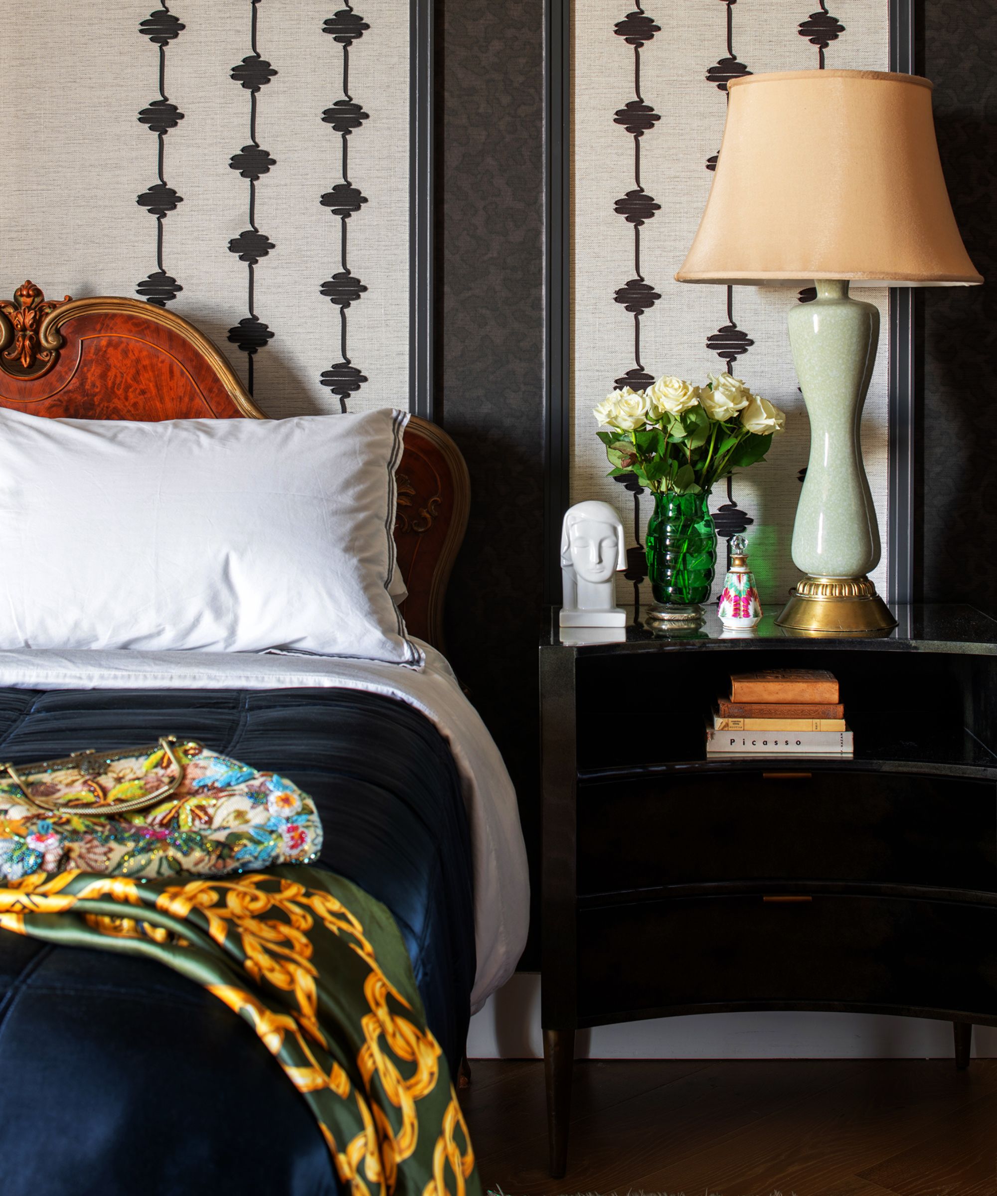 A bedroom with panelled walls with black wallpaper, a dark nightstand, and traditional decor.